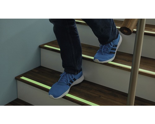 Personne montant un escalier avec des bandes antidérapantes.