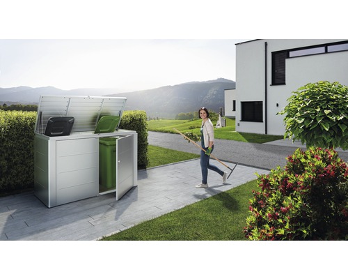 Mülltonnenbox im Garten mit einer Frau mit Gartengerät