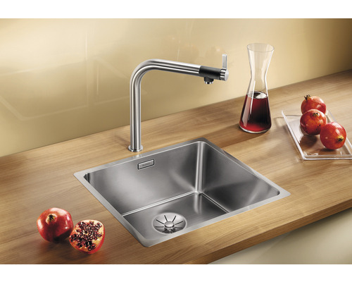 Évier en acier inoxydable avec robinet et grenades sur un plan de travail en bois.