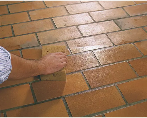 Une personne nettoie des carreaux de sol avec une éponge