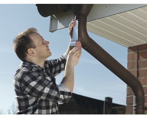 Un homme répare une gouttière avec du ruban adhésif.