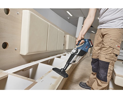 Eine Person verwendet einen Akku-Staubsauger zur Reinigung eines Holzregals.