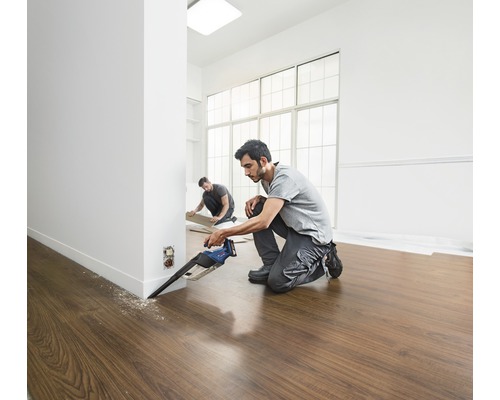 Zwei Handwerker verlegen Laminatboden mit einer Tauchsäge in einem hellen Raum.