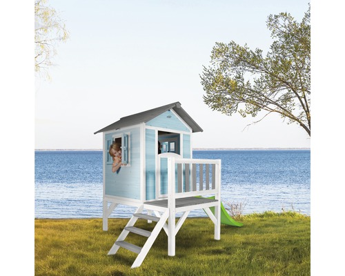 Spielhaus mit Rutsche, Treppe und Fenster auf einer Rasenfläche vor einem See