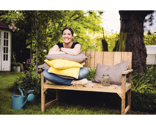 Frau sitzt auf Holzbank mit Kissen im Garten