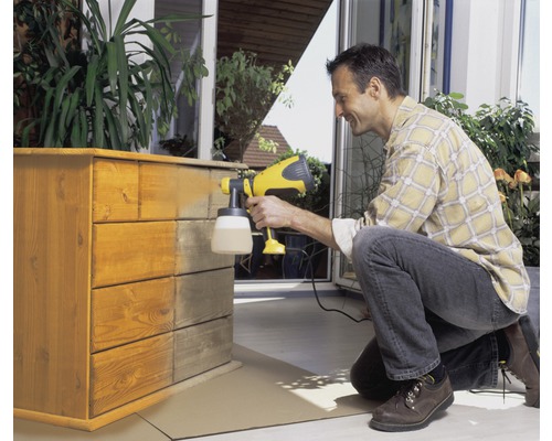 Un homme vaporise une commode en bois avec un pistolet à peinture.