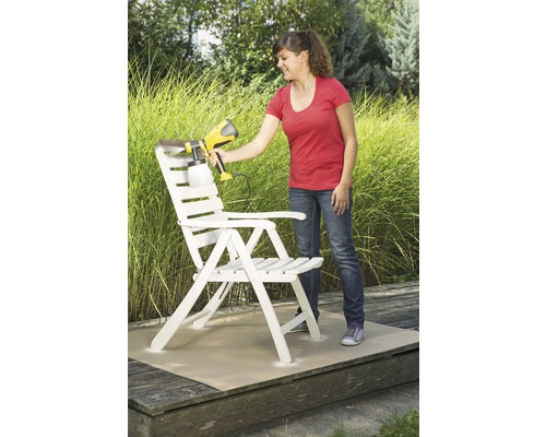 Une femme peint une chaise en bois avec un pistolet à peinture dans le jardin.
