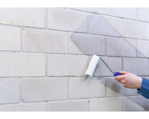 Une personne peint un mur de briques avec un rouleau à peinture.