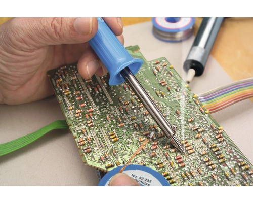 Une personne soude une carte de circuit imprimé avec un fer à souder. De la soudure est également présente.