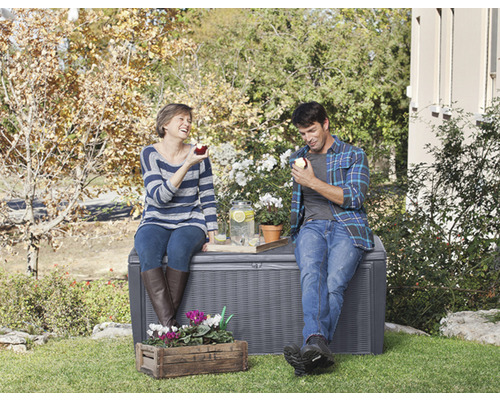 Un couple est assis sur un coffre de jardin gris à l''extérieur et mange des pommes.