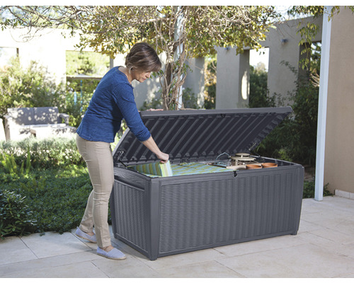 Femme ouvrant un coffre de jardin gris pour ranger le matériel de jardinage et les coussins à l''extérieur.