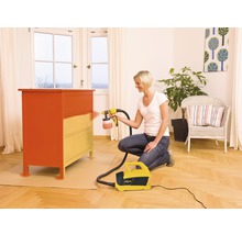 Femme peint une commode avec un système de pulvérisation de peinture dans un salon.