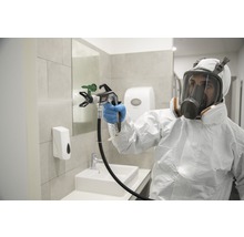 Une personne en tenue de protection utilise un pulvérisateur de peinture dans une salle de bain.