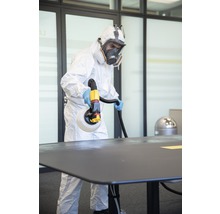 Une personne en équipement de protection désinfecte une table avec un pulvérisateur de désinfectant.