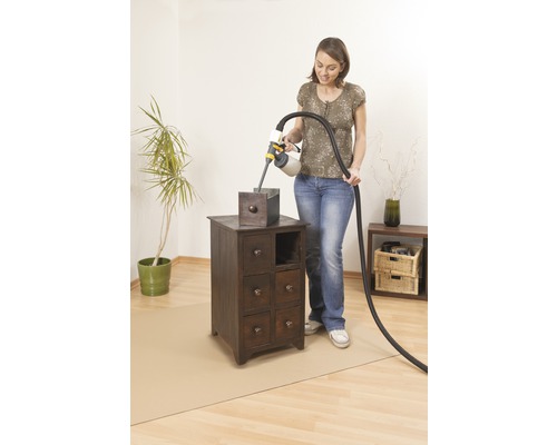 Une femme vernit une table de chevet avec un système de pulvérisation de peinture