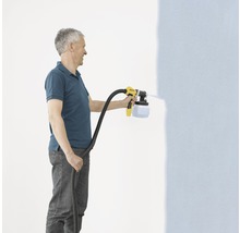 Un homme utilise un pulvérisateur de peinture pour peindre un mur.