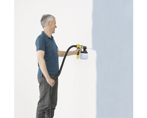 Un homme utilise un pulvérisateur de peinture pour peindre un mur.