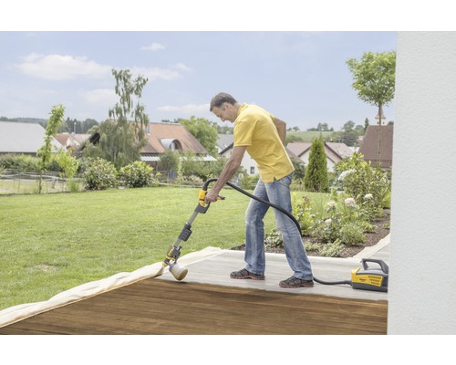 Un homme traite une terrasse en bois avec un système de pulvérisation de peinture Wagner dans le jardin.