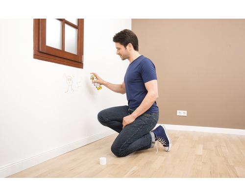 Un homme enlève des dessins d''un mur avec de la peinture en aérosol dans une pièce.