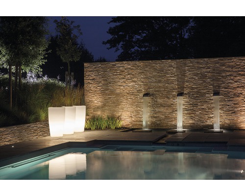 Beleuchteter Garten mit Pool, Steinmauer, Pflanzkübeln und Wasserspielen bei Nacht