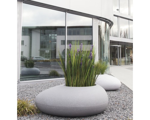 Pots de fleurs décoratifs aspect pierre avec des plantations devant un bâtiment moderne