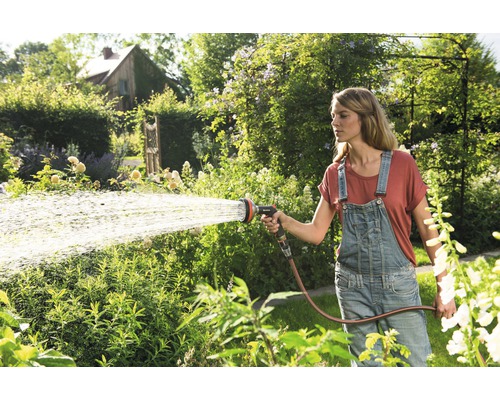 Frau gießt Garten mit Gartenschlauch und Sprühkopf