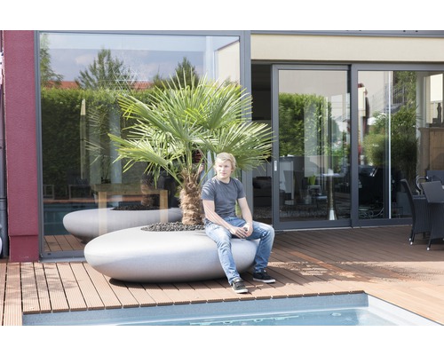 Extérieur avec piscine et homme assis sur un bac à fleurs avec palmier