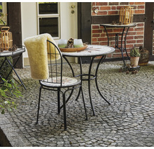 Gartenszene mit Mosaiktisch, Stuhl mit Fellauflage und Beistelltisch auf gepflastertem Untergrund