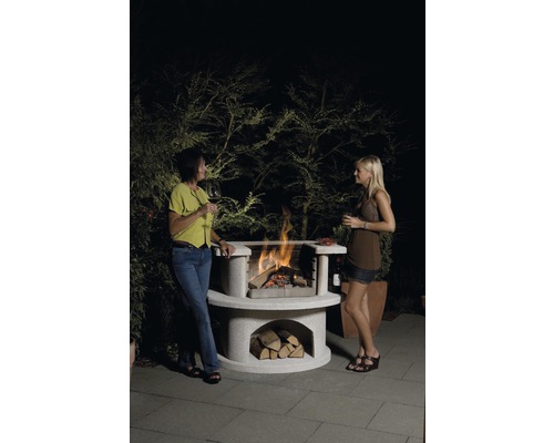 Zwei Frauen stehen an einem Steingrill mit Holz und Feuer.