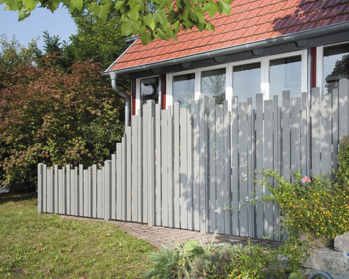 Holzzaun mit unregelmäßiger Oberkante vor einem Haus