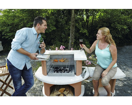 Un homme et une femme font des grillades dans le jardin avec un barbecue en pierre et du charbon de bois.