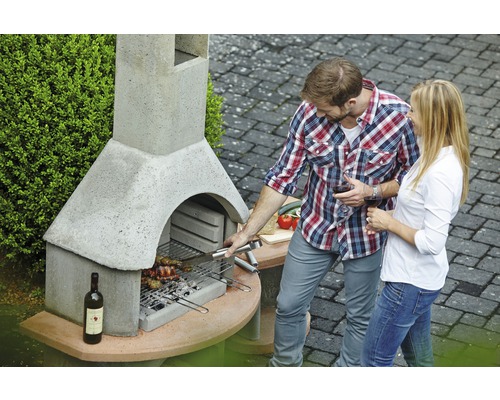 Mann und Frau grillen an einem Gartengrill aus Stein mit Flasche Wein