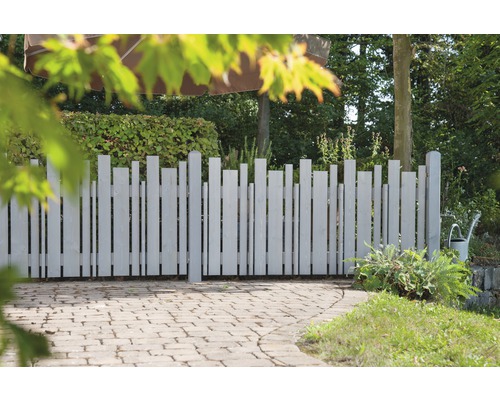 Clôture en bois avec des lattes verticales de différentes hauteurs dans le jardin