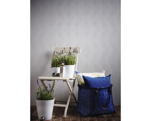 Dekorative Szene mit Blumentöpfen auf einem Klappstuhl vor einer gemusterten Tapete und einem geflochtenen Korb mit Kissen.