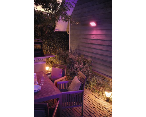 Terrasse éclairée avec table en bois, chaises et barbecue