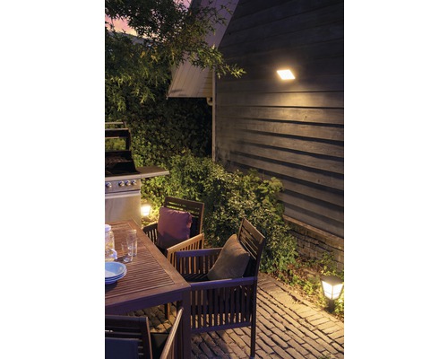Espace extérieur avec table de jardin, chaises, barbecue et éclairage extérieur.
