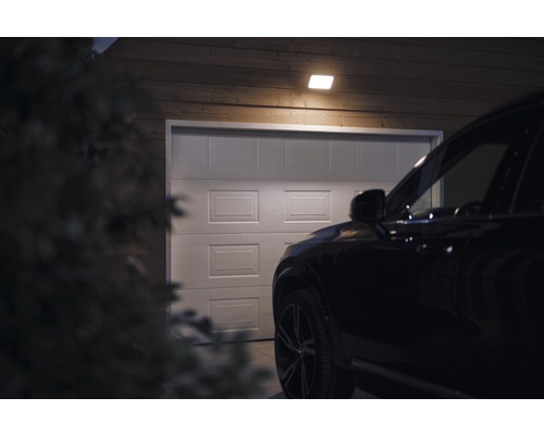 Scène avec un garage, éclairé par un plafonnier, avec une voiture devant.