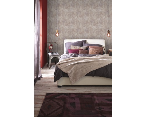 Schlafzimmer mit gemusterter Tapete, Bett, Teppich und dekorativen Elementen für eine gemütliche Atmosphäre.