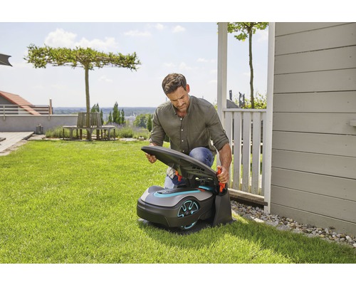Ein Mann öffnet einen Rasenmähroboter in einem Garten.
