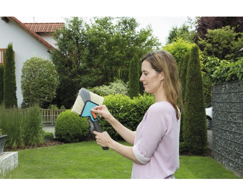 Une femme tient une brosse pour nettoyer les surfaces dans le jardin