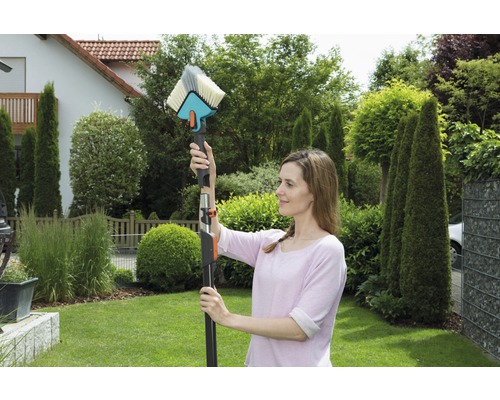 Une femme utilise une brosse de lavage avec manche télescopique pour nettoyer dans le jardin.