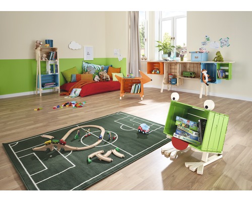 Ein Kinderzimmer mit einem Bett, Regalen aus Holzkisten und einem grünen Teppich mit Fußballfeldmuster.