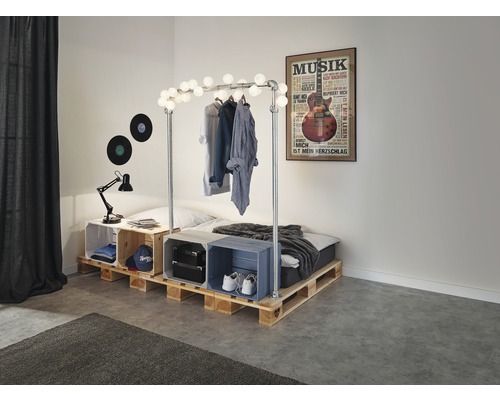 Schlafzimmer mit Bett aus Holzpaletten, dekoriert mit einer Lichterkette und einem Musikposter