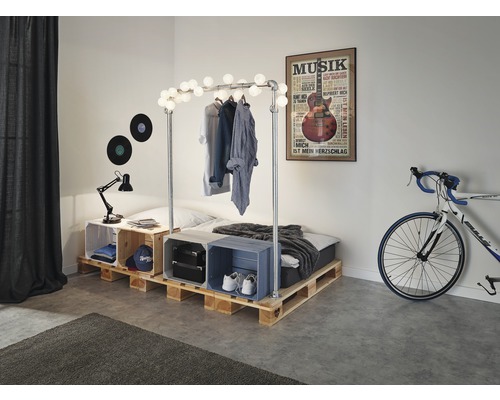 Schlafzimmer mit Palettenbett, Kleiderständer mit Beleuchtung und dekorativen Kisten