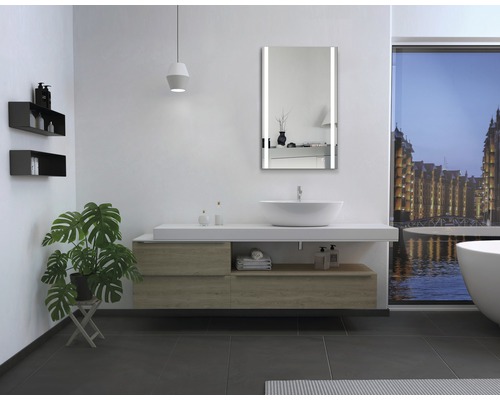 Modernes Badezimmer mit Waschtisch, beleuchtetem Spiegel und Badewanne vor einem Fenster