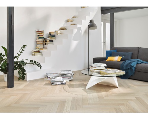 Wohnzimmer mit hellem Fischgrätparkett, Treppe mit Büchern und grauer Couch