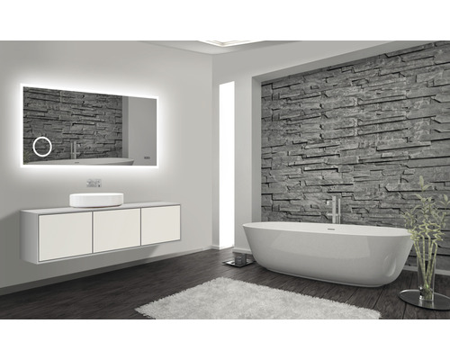 Salle de bains moderne avec miroir lumineux, meuble-lavabo, vasque à poser et baignoire îlot devant un mur en pierre