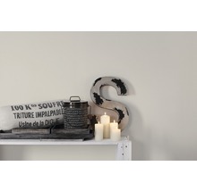 Scène décorative avec coussin, boîte, bougies et une grande lettre sur une étagère.