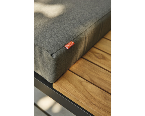 Vue détaillée d''un coussin d''assise gris sur une table de jardin avec une surface en bois et un cadre noir.