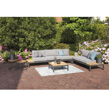 Ensemble de meubles de jardin avec canapé, chaise longue, table basse et tables d''appoint sur une terrasse avec des fleurs en arrière-plan.